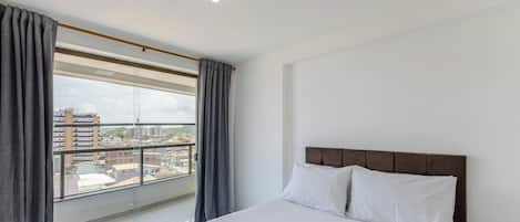A hotel room with a large window, a bed with white bedding, and a view of the cityscape.