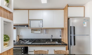 Una cocina compacta con gabinetes blancos, un microondas integrado, un refrigerador de acero inoxidable, una estufa a gas y un horno empotrado.