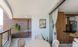 Un balcón moderno con pared de ladrillo, puerta de cristal y zona de comedor con mesa y sillas redondas.