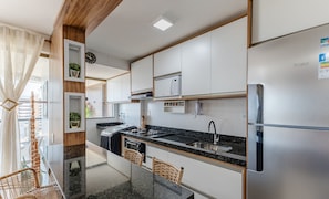 Una cocina moderna con armarios blancos, encimera negra y microondas integrado. Hay sillas de mimbre y una pequeña mesa de comedor.