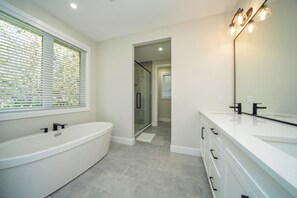 Een moderne badkamer met een vrijstaand bad, een grote spiegel en een ruime douche.