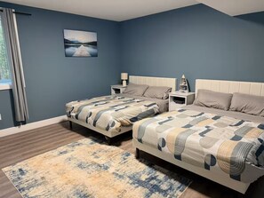 A bedroom with two beds, a nightstand, a lamp, and a painting on the wall. - Executive Cottage on Lakeview HotTub Firepit Sauna Nearby Walking Nature Trails (Lambton Shores)
