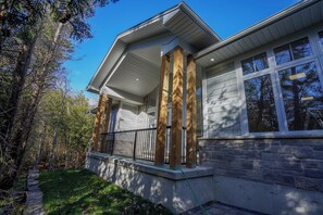 Une maison avec une façade en pierre, un porche en bois doté de colonnes et une balustrade noire.