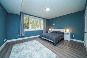 Een slaapkamer met een bed, twee nachtkastjes, een raam met gordijnen, een wit tapijt en een plafondlamp.