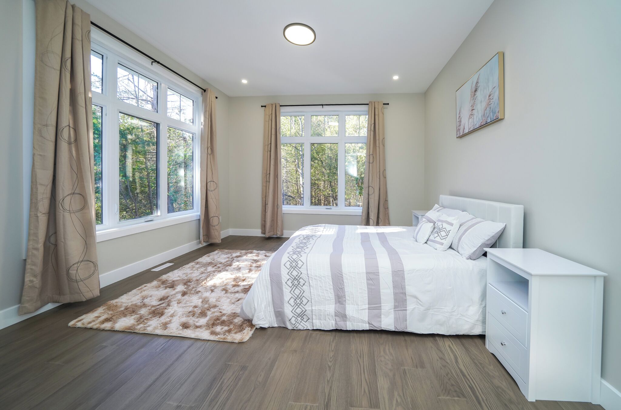 Un dormitorio con cama, mesita de noche y vistas a árboles a través de amplios ventanales.