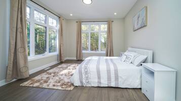 Un dormitorio con cama, mesita de noche y vistas a árboles a través de amplios ventanales.