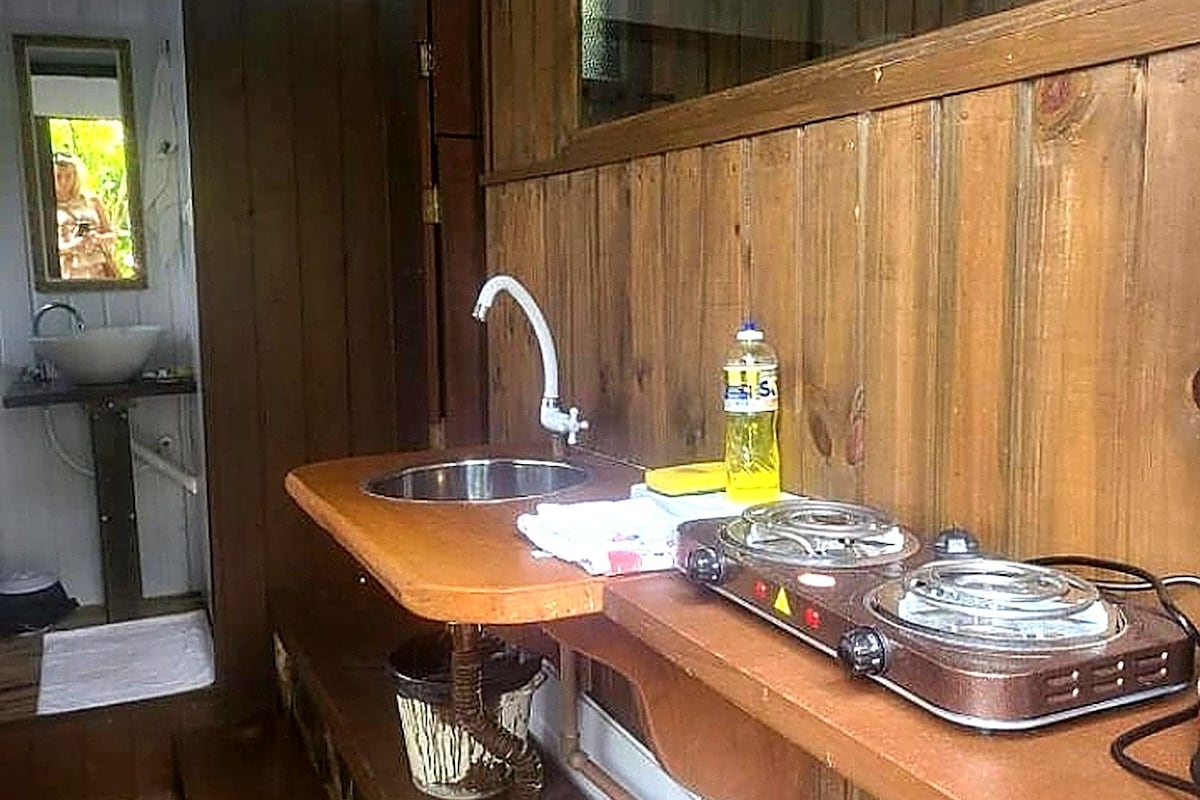 A wooden cabin interior with a kitchen area featuring a sink, a stove, and a window.