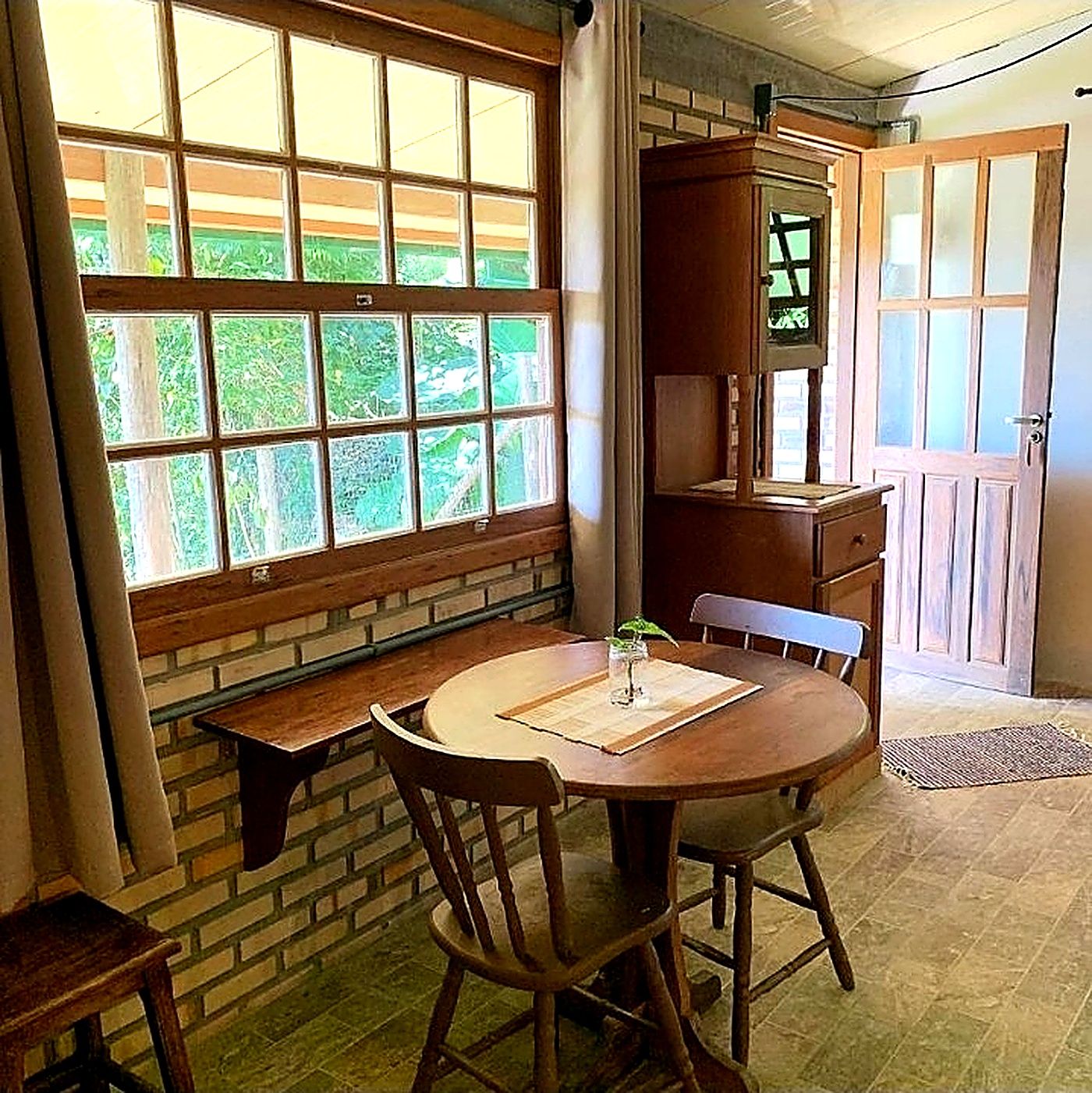 Un comedor con una mesa redonda, dos sillas, un banco y una ventana con vistas a la vegetación.