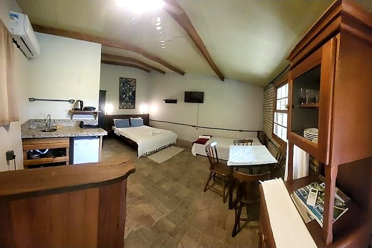 A compact room with a kitchenette, a bed, a dining table, and a wooden cabinet.