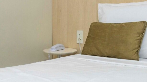 Een hotelkamer met een bed, een nachtkastje met een telefoon en een stopcontact.