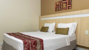 Een hotelkamer met een bed, wit beddengoed, een rode en gouden plaid en een houten hoofdeinde.