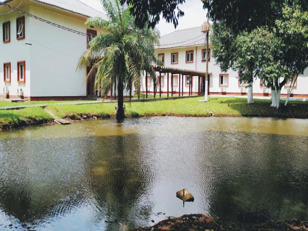 Ein Gebäude mit weißer Fassade und rotem Zierstreifen, einer überdachten Außenfläche und einem Teich mit einem Vogel.