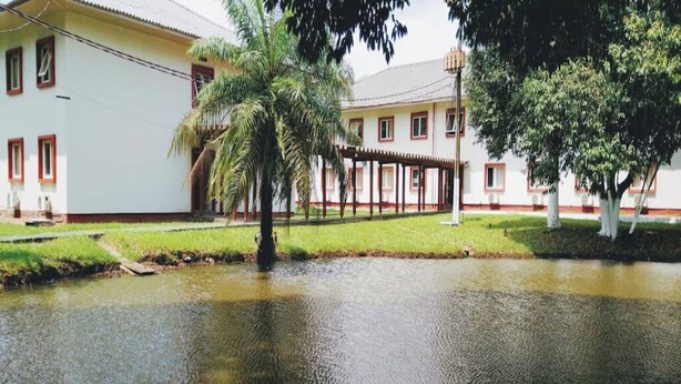 A building with a white facade and red trim, a covered outdoor area, and a pond with a bird. - Peaceful, Airy Unit in a Prime Location Near Belém’s Highlights + Pool Access (Pará)