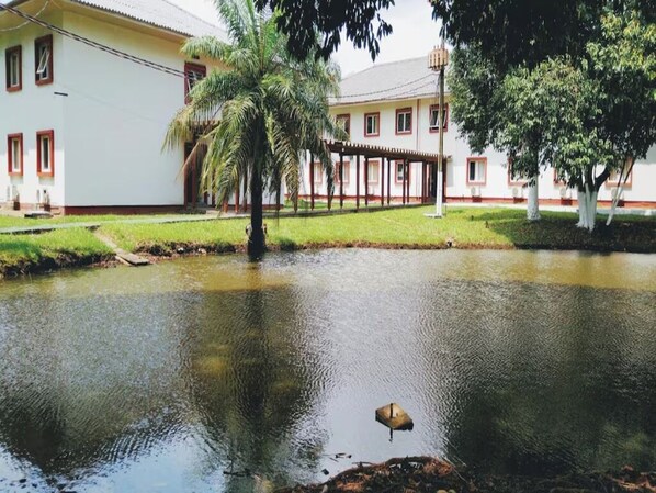 A building with a white facade and red trim, a covered outdoor area, and a pond with a bird. - Peaceful, Airy Unit in a Prime Location Near Belém’s Highlights + Pool Access (Pará)