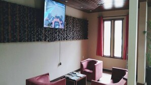 Una habitación moderna con una televisión de pantalla plana montada en la pared, una pequeña mesa con libros y dos sillas rojas.