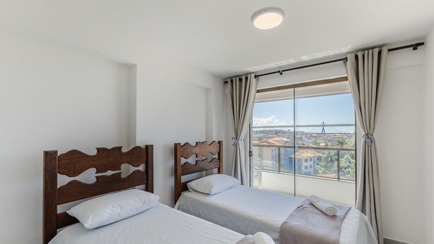 A hotel room with two beds, a large window with curtains, and a view of a cityscape and bridge.