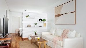 Una sala moderna con un sofá blanco, una mesa de centro, un televisor y una estantería con plantas.