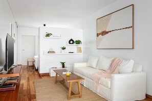 Una sala moderna con un sofá blanco, una mesa de centro, un televisor y una estantería con plantas.