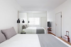 Una habitación de hotel moderna con cama, mesitas de noche, televisor y armario.