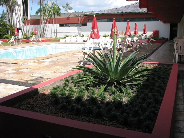 A pool area with lounge chairs and umbrellas, surrounded by a garden with plants and a palm tree. - Peaceful Retreat Designed for Quiet & Restful Stays w/ Pool & Lake Access (Pará)