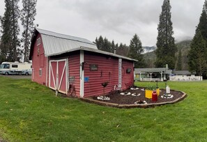 Ein rotes Bauernhaus mit einem Metalldach, einem weißen Zaun und einem Garten mit Pflanzen und einem Vogelhäuschen.