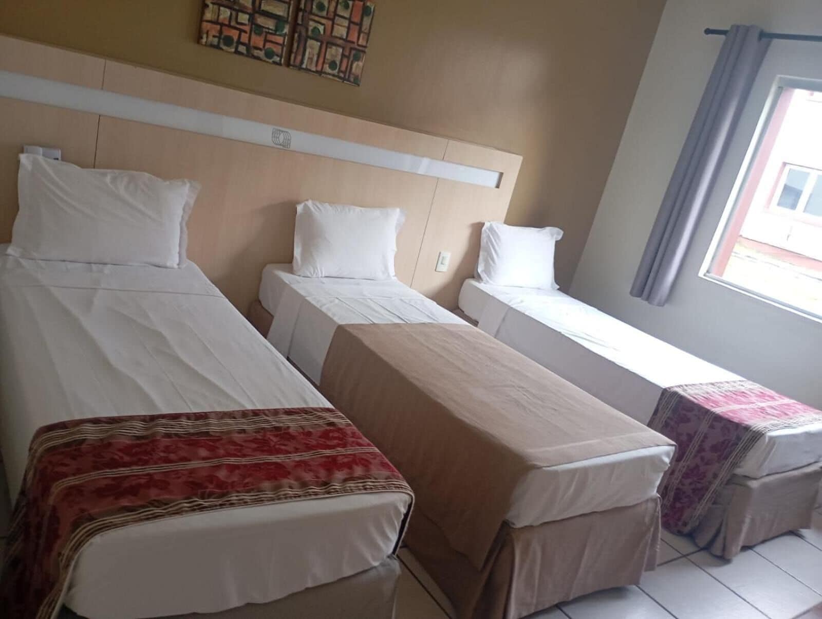Ein Hotelzimmer mit zwei Einzelbetten, einem kleinen Tisch und einem Fenster mit Vorhängen.