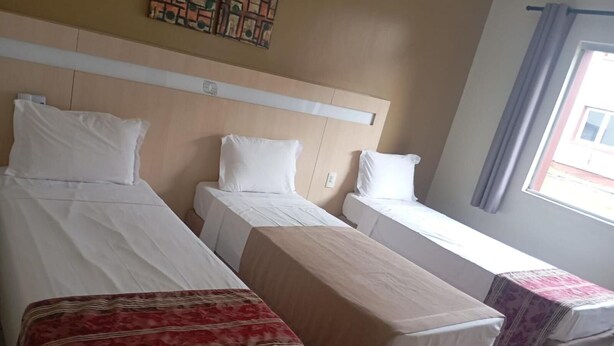 Ein Hotelzimmer mit zwei Einzelbetten, einem kleinen Tisch und einem Fenster mit Vorhängen.