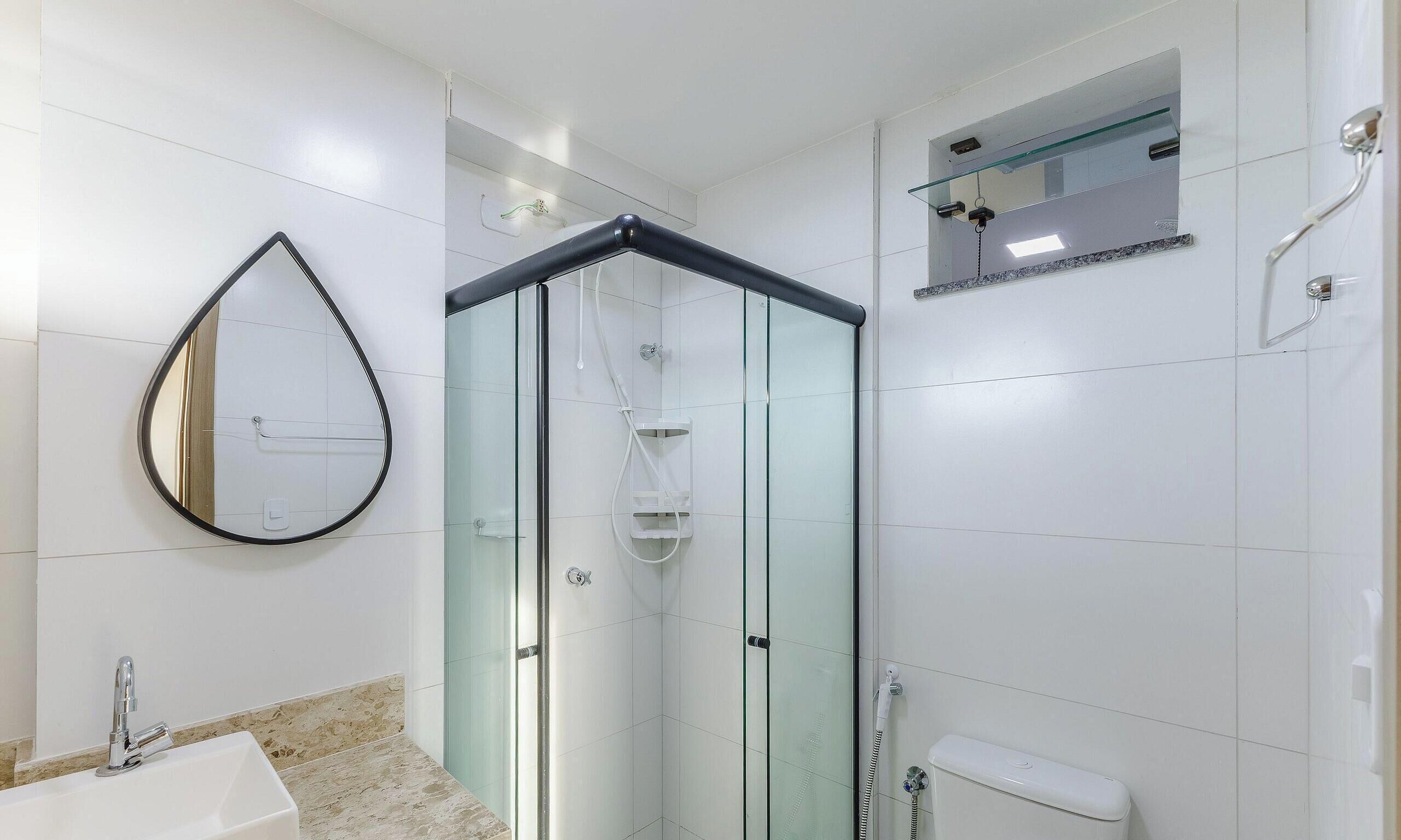 A modern bathroom with a glass-enclosed shower, a round mirror, a white sink, and a toilet.