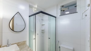 A modern bathroom with a glass-enclosed shower, a round mirror, a white sink, and a toilet. - Stay Near sea w/ Pool & Balcony Mmd0604 (Ilhéus)