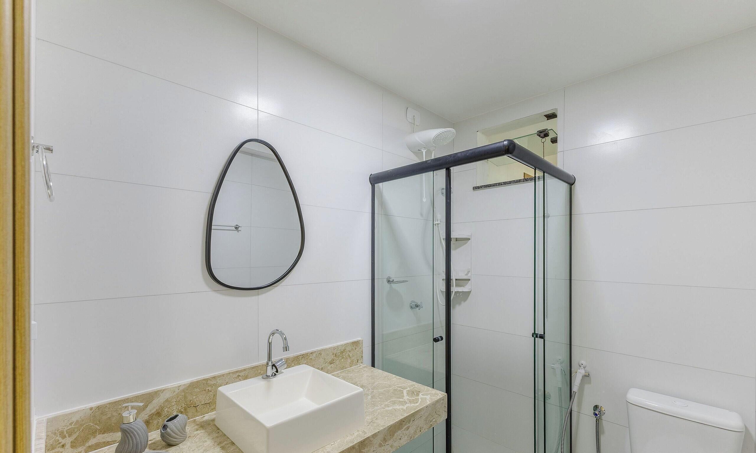 A modern bathroom with a glass-enclosed shower, a white sink with a marble countertop, and a large oval mirror.