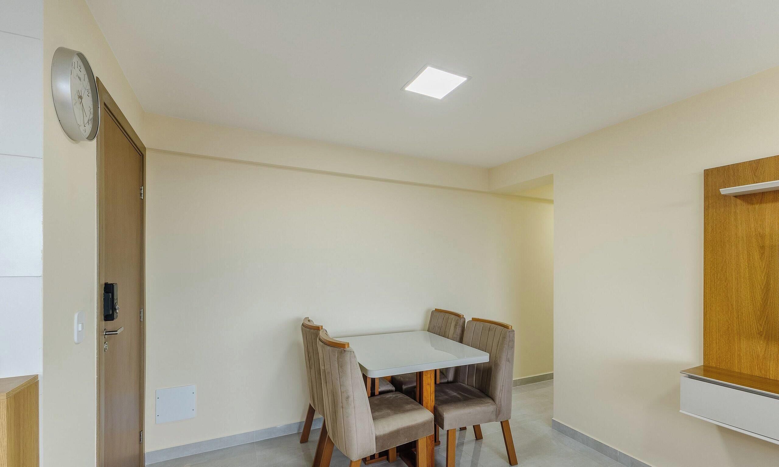 A room with a dining table and four chairs, a clock on the wall, and a recessed ceiling light.