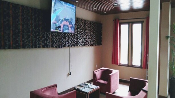 Habitació moderna amb televisió de pantalla plana penjada a la paret, una taula petita amb llibres i dues cadires vermelles.