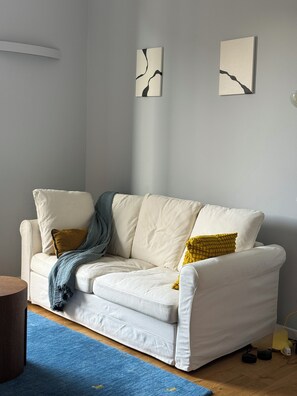A white sofa with a blue throw blanket and yellow pillows, a blue rug, and two abstract wall art pieces. - La Dolce Vita - Vintage Two-Room Apartment in Dateo (Milano)