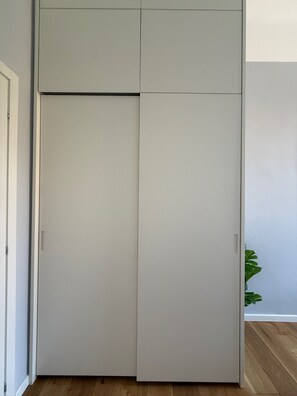 Ein geschlossener grauer Kleiderschrank mit Griff, ein Holzboden und eine Pflanze in der Ecke.