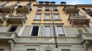 Ein mehrstöckiges Gebäude im klassischen Stil, mit aufwendigen Balkonen und einem zentralen Eingang, an dem die Nummer 64 angebracht ist.