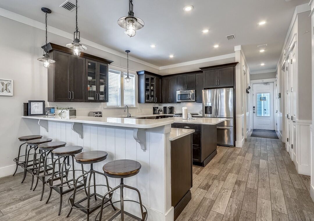A modern kitchen with dark cabinets, a central island with stools, and stainless steel appliances.