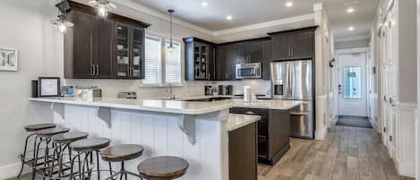 A modern kitchen with dark cabinets, a central island with stools, and stainless steel appliances.