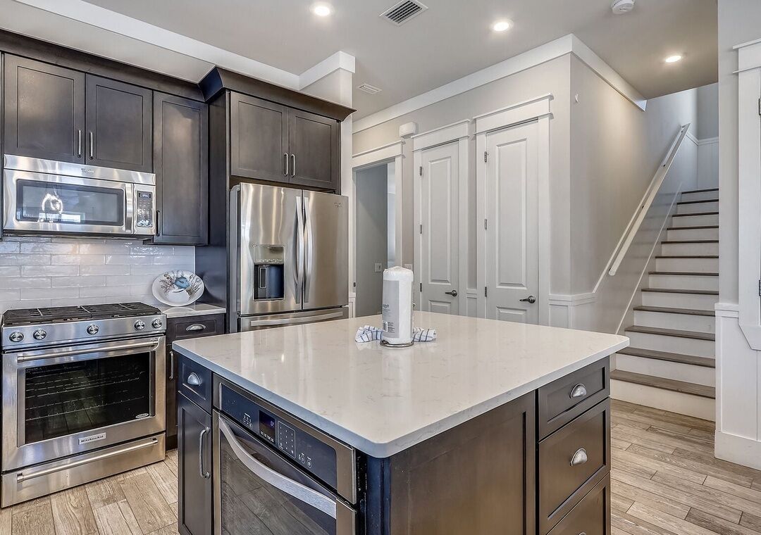 A modern kitchen with stainless steel appliances, a central island, and a staircase leading to another level.