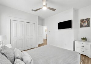 A bedroom with a bed, a ceiling fan, a TV, a dresser, and a door leading to another room. - Lucky Snapper - 30A Coastal Retreat with 6-Seater Golf Cart (Santa Rosa Beach)