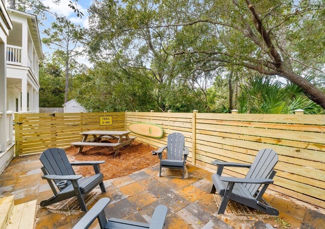 An outdoor patio with Adirondack chairs, a picnic table, and a wooden fence.