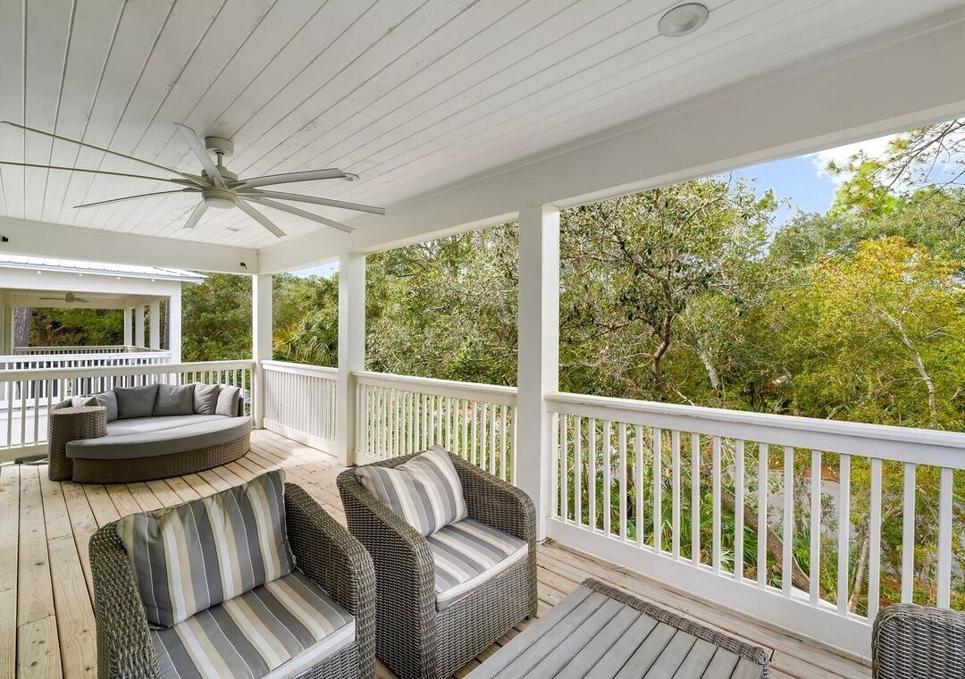 A covered outdoor deck with wicker furniture and a ceiling fan.