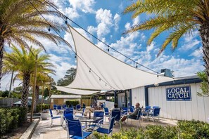 An outdoor seating area with blue chairs and a white canopy, a sign reading 'LOCAL CATCH BAR & GRILL,' and palm trees in the background. - Lucky Snapper - 30A Coastal Retreat with 6-Seater Golf Cart (Santa Rosa Beach)