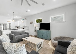 A modern living room with a grey sofa, a wooden coffee table, and a television on a teal cabinet. - Lucky Snapper - 30A Coastal Retreat with 6-Seater Golf Cart (Santa Rosa Beach)