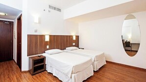 Quarto de hotel com duas camas, piso de madeira, um espelho e uma pequena escrivaninha.