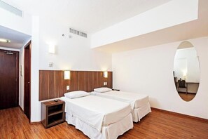Een hotelkamer met twee bedden, een houten vloer, een spiegel en een klein bureau.