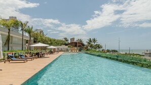 A swimming pool with lounge chairs and umbrellas, surrounded by greenery and buildings. - Apt w/ Balcony, BBQ & sea View Shc0801 (Picarras)