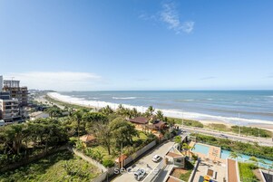 Vista costera con playa, océano y una carretera que conduce a un edificio con piscina y vistas al mar.