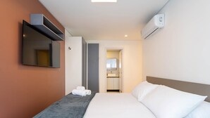 A hotel room with a bed, a flat-screen TV mounted on the wall, a built-in air conditioning unit, and a bathroom visible through an open door. - Apt w/ Balcony, BBQ & sea View Shc0801 (Picarras)