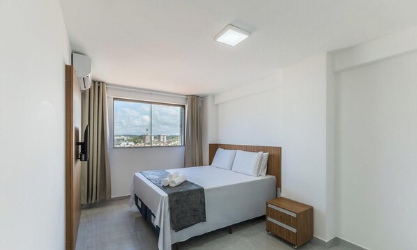 A hotel room with a bed, a nightstand, a window with curtains, and a view of buildings. - Apt. With sea View in Bldg. With Pool Mmd0605 (Ilhéus)