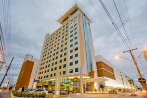 A multi-story hotel with a prominent entrance, a large glass facade, and a rooftop structure. - Prime Location in Palhoça | Work-Friendly Unit | Pets Allowed (Santa Catarina)